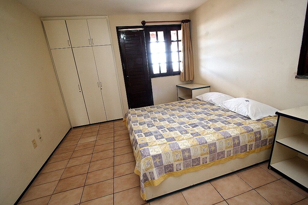 Un dormitorio con cama, armario, mesita de noche y ventana con cortinas.