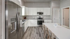 A modern kitchen with white cabinets, stainless steel appliances, and a wooden floor.