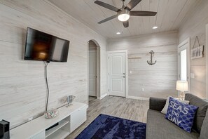 A modern living room with a flat-screen TV, a ceiling fan, and a blue rug. - Copano Breeze 3 Bedroom Home by RedAwning (Rockport)