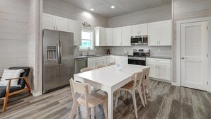 A modern kitchen with white cabinetry, stainless steel appliances, and a central island with chairs.