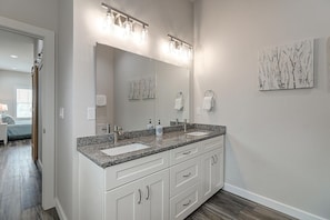 A bathroom with a double sink vanity, a large mirror, and a wall-mounted light fixture. - Copano Breeze 3 Bedroom Home by RedAwning (Rockport)