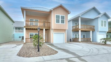A multi-story residential building with a central garage, a balcony on the second floor, and a small landscaped area with a street lamp.