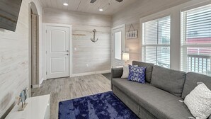 A spacious living room with a grey sofa, a blue rug, and a ceiling fan.