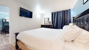 A neatly made bed with white linens, a dark headboard, and a flat-screen TV mounted on the wall. - Krystal Villas East 312 Quaint and Cozy, Great Value for your Mammoth Getaway by RedAwning (Mammoth Lakes)