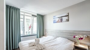 A hotel room with a large bed, a nightstand, a vase with flowers, and a painting on the wall. - Spacious and luxurious apartment - Kaag Resort (22) (Warmond)