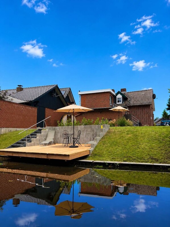 A residential area with a wooden deck, outdoor seating, and a clear reflection in the water.