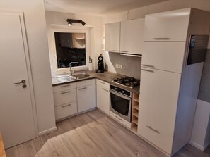 Une cuisine compacte avec des meubles blancs, un évier en acier inoxydable, une cuisinière à gaz et un four encastré.