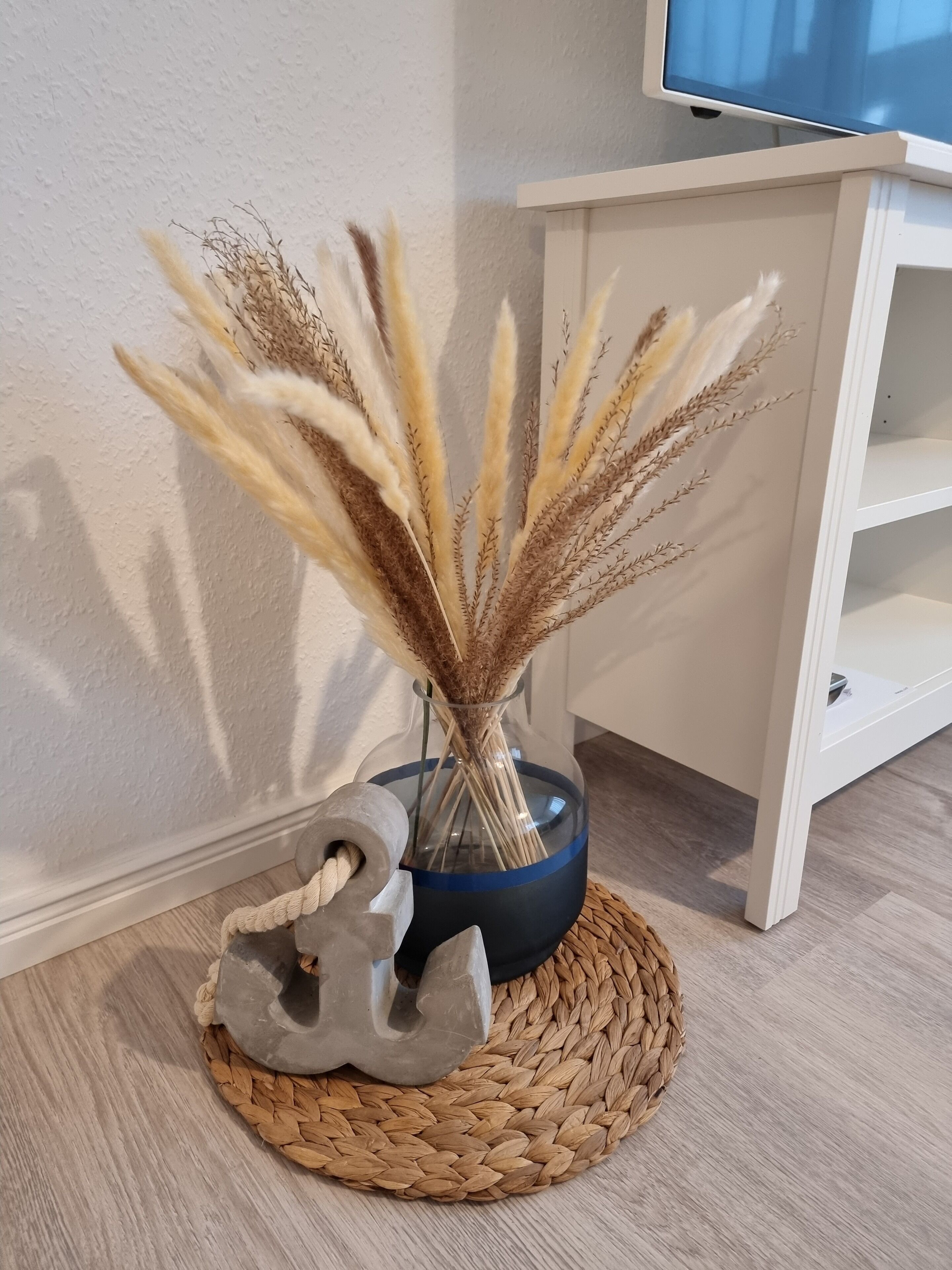 A decorative vase with dried plants on a woven mat, a stone sculpture, and a white shelf unit.