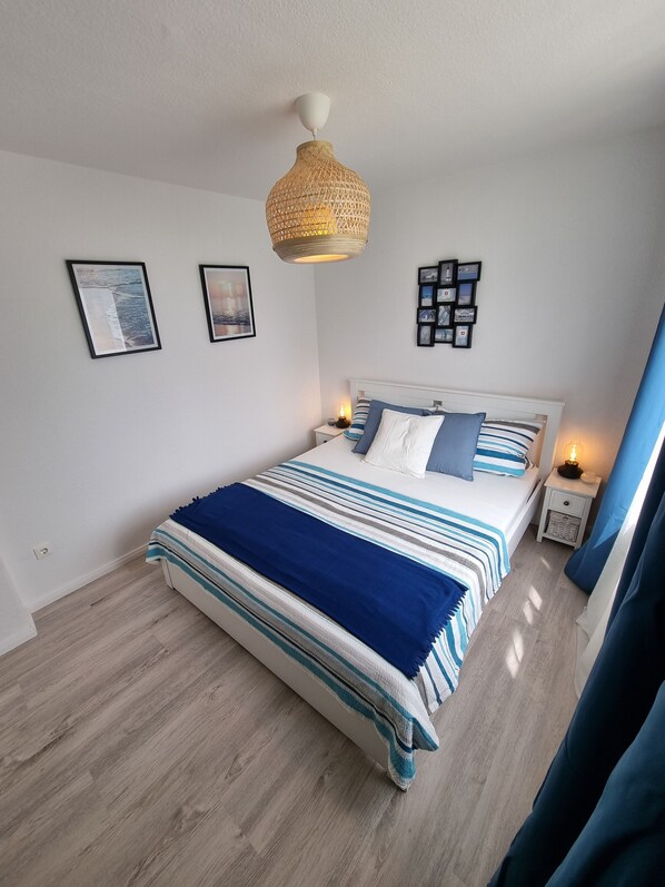 Une chambre à coucher comprenant un lit, une table de chevet, une commode, un luminaire suspendu et des tableaux encadrés accrochés au mur.