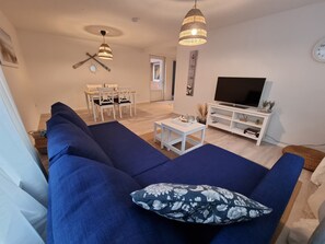 Un salon avec un canapé bleu, un meuble TV blanc et un coin repas comprenant une table et des chaises.