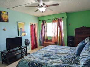 A bedroom with a bed, a TV, a ceiling fan, and curtains.