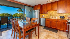 A modern kitchen with wooden cabinets, a stainless steel refrigerator, and a granite countertop. - Maui Parkshore #412 Ocean View in the Heart of Kihei, Walk to Kamaole Beach (Kihei)