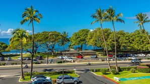 A parking lot with cars, palm trees, and a view of the ocean. - Maui Parkshore #412 Ocean View in the Heart of Kihei, Walk to Kamaole Beach (Kihei)