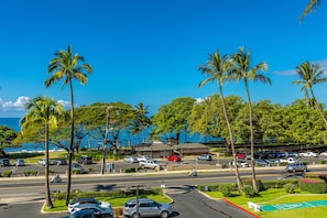 A parking lot with cars, palm trees, and a view of the ocean. - Maui Parkshore #412 Ocean View in the Heart of Kihei, Walk to Kamaole Beach (Kihei)