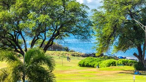 A golf course with a view of the ocean, surrounded by trees and greenery. - Maui Parkshore #412 Ocean View in the Heart of Kihei, Walk to Kamaole Beach (Kihei)