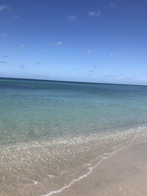 A beach with clear shallow waters and a sandy shore.