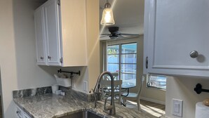A kitchen with a marble countertop, stainless steel sink, white cabinets, and a ceiling fan. - Private heated pool. Shark teeth, close to beaches, downtown, shopping, biking… (Venice)