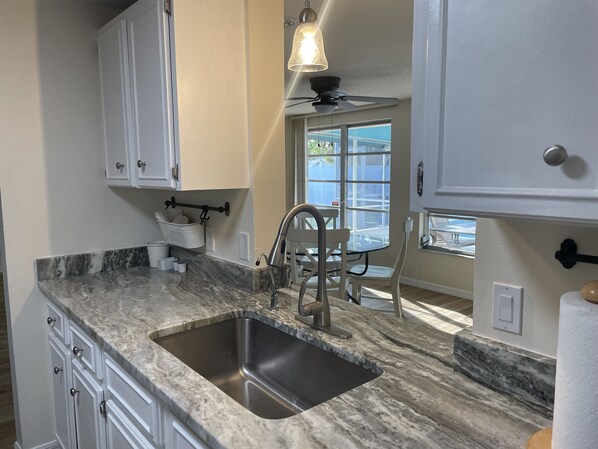 A kitchen with a marble countertop, stainless steel sink, white cabinets, and a ceiling fan.