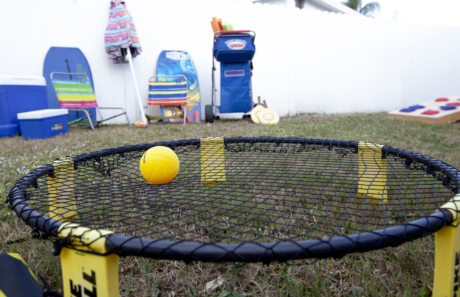 Un filet de volley-ball avec un ballon au centre, entouré d’une zone herbeuse, avec divers objets en arrière-plan.