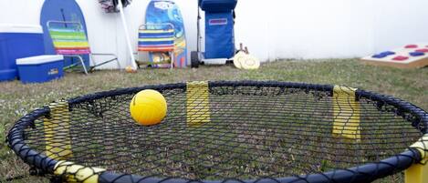Un filet de volley-ball avec un ballon au centre, entouré d’une zone herbeuse, avec divers objets en arrière-plan.