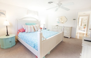 Quarto com cama, penteadeira, mesa de cabeceira e ventoinha no teto.
