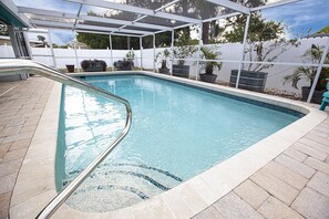 Ein Schwimmbecken mit einer gefliesten Kante, einer Metallleiter und Pflanzen in Töpfen entlang des Randes.