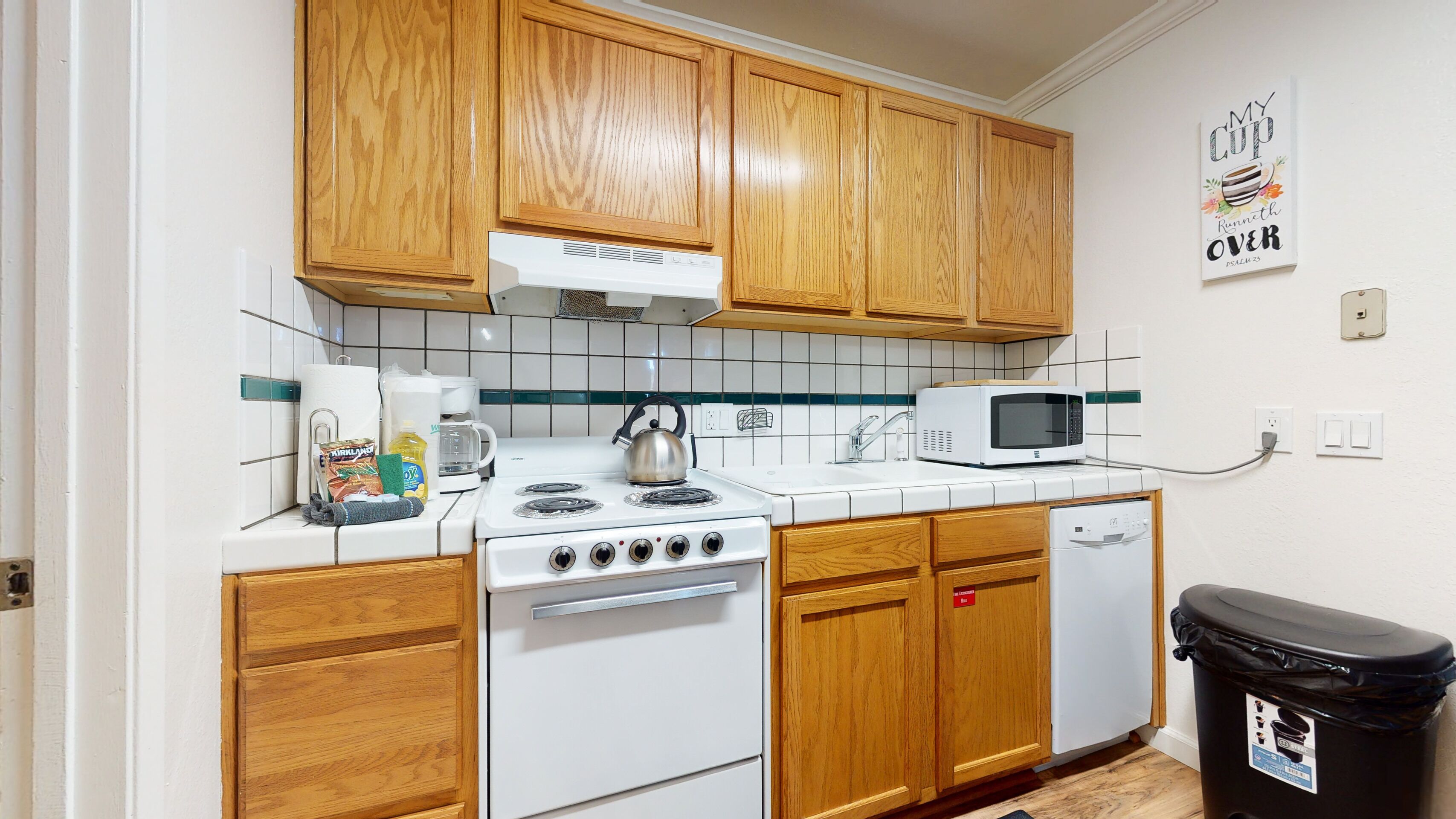 A kitchen with wooden cabinets, a stove, a microwave, and a trash bin.