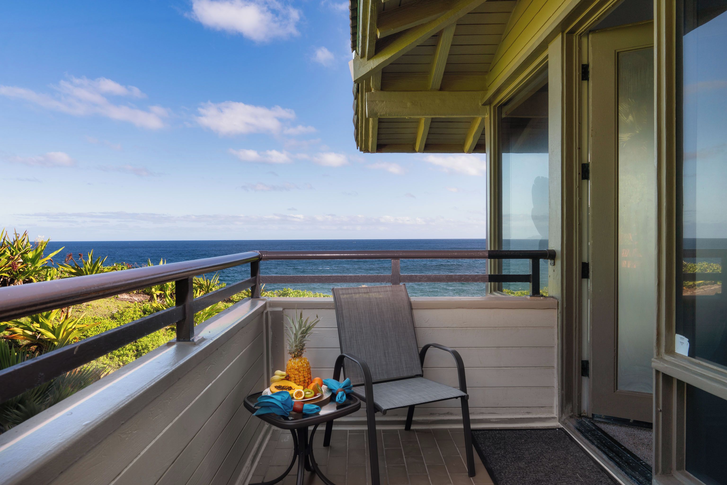 A balcony with a view of the ocean, a table with fruits, and a chair.
