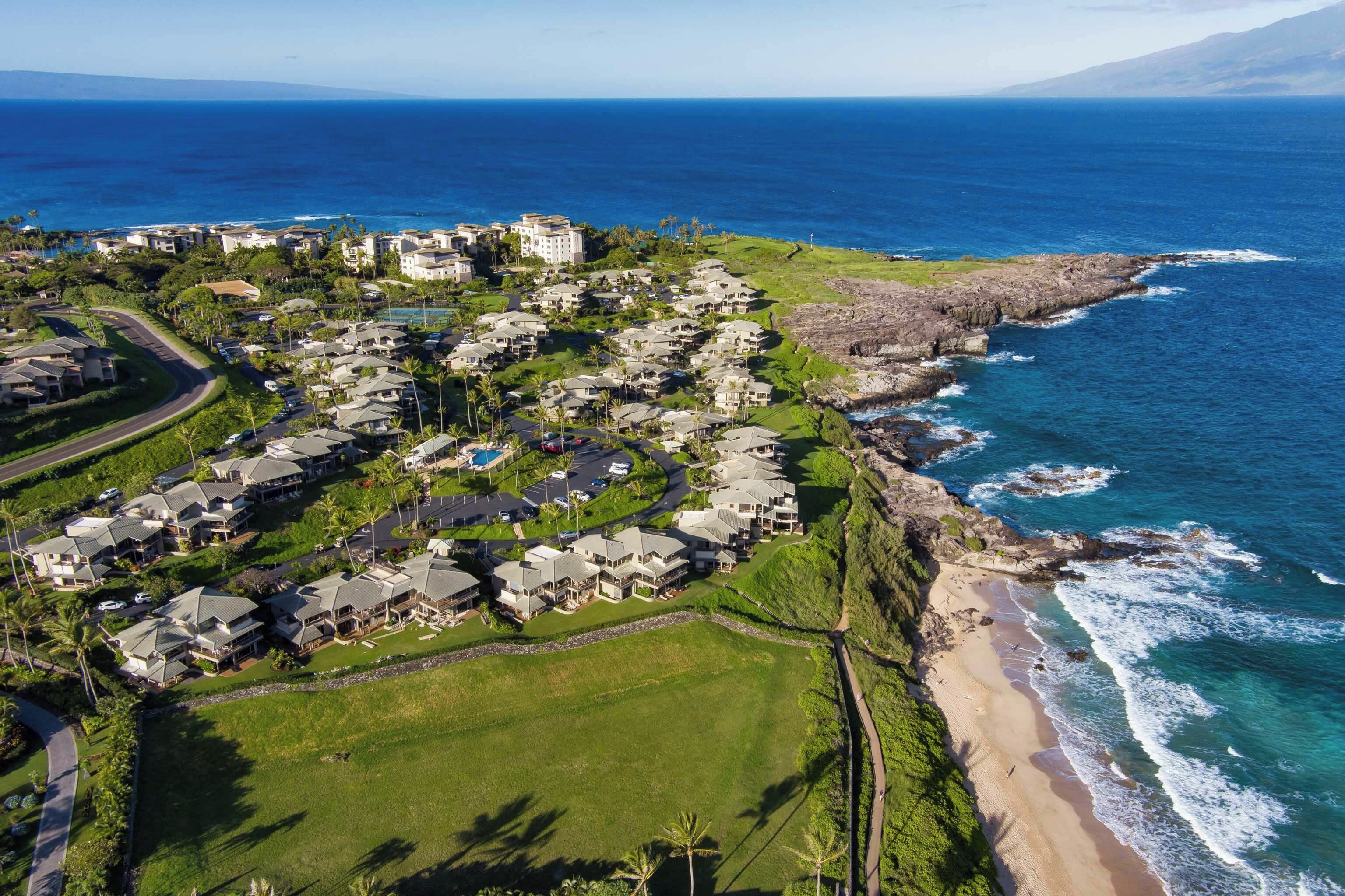 A coastal residential area with houses along the beach, a clear view of the ocean, and a road curving through the property.