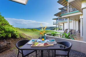 An outdoor dining area with a table set for two, overlooking a scenic view of the ocean and hills.