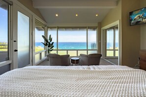 A bedroom with a large bed, a view of the ocean, and two chairs by a window.