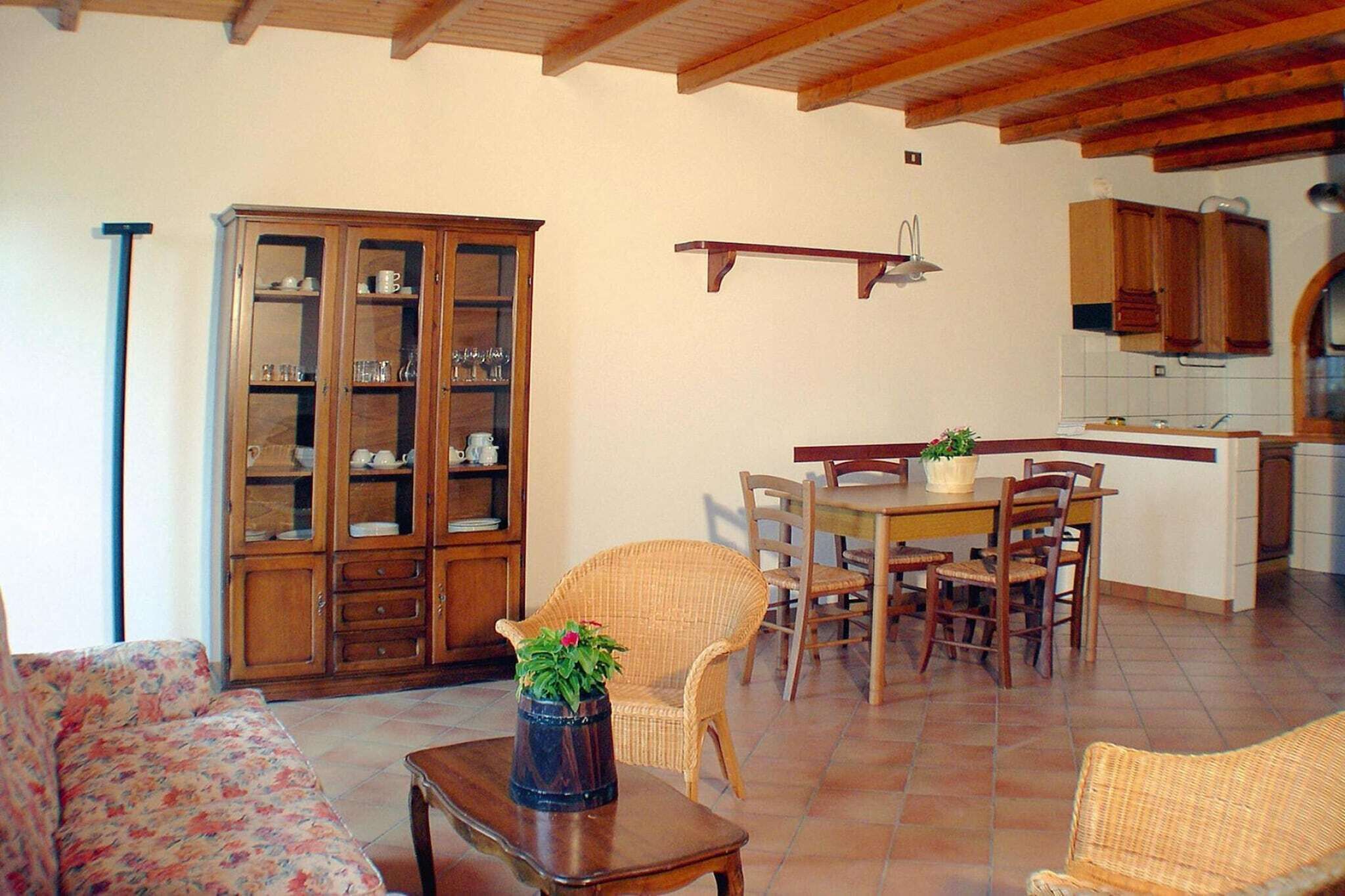 A living room with a sofa, a dining table with chairs, a cabinet, and a kitchen area with cabinets and a window.