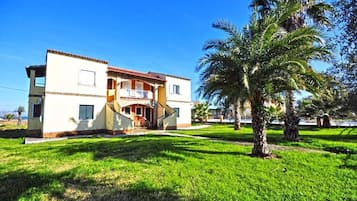 Una casa de dos pisos con balcón, rodeada de un césped cuidado y palmeras.