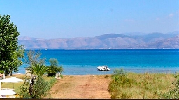 A coastal view with a clear sky, a sandy path leading to the sea, and distant mountains. - Summer Desire (Corfu)
