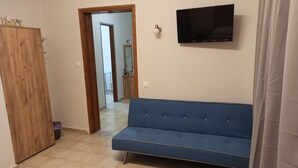 A room with a blue sofa, a wooden wardrobe, a flat-screen TV, and a bathroom visible through an open door. - Summer Desire (Corfu)