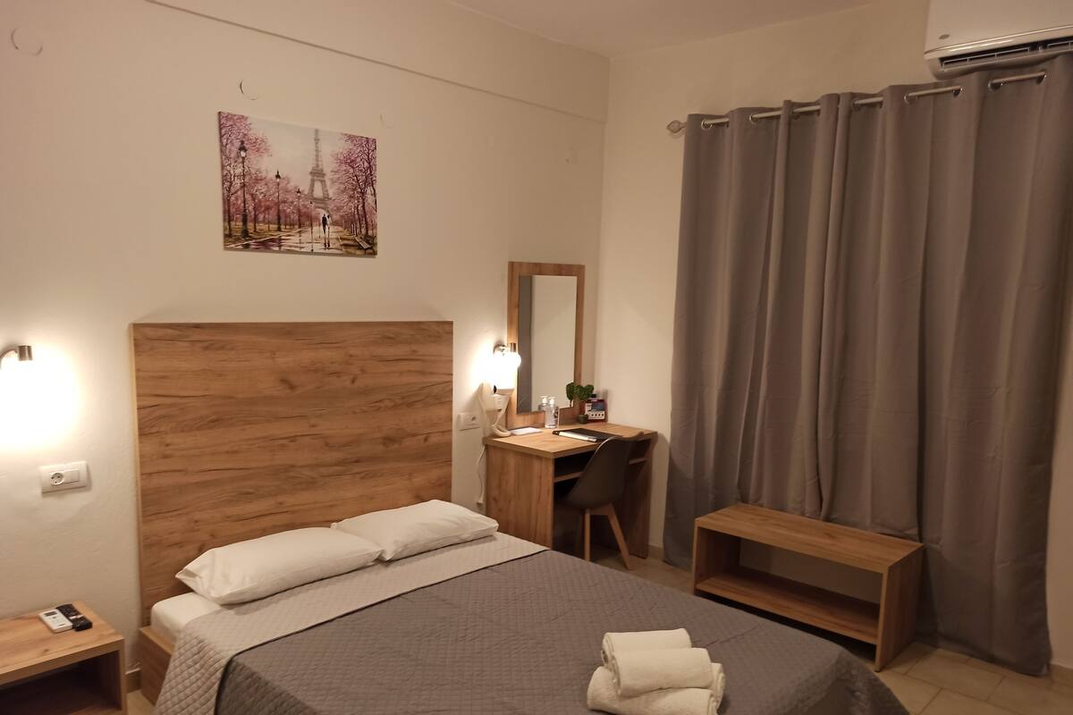 Quarto bem organizado com cabeceira de madeira, escrivaninha, cadeira, mesa de cabeceira e cama com colcha acolchoada.