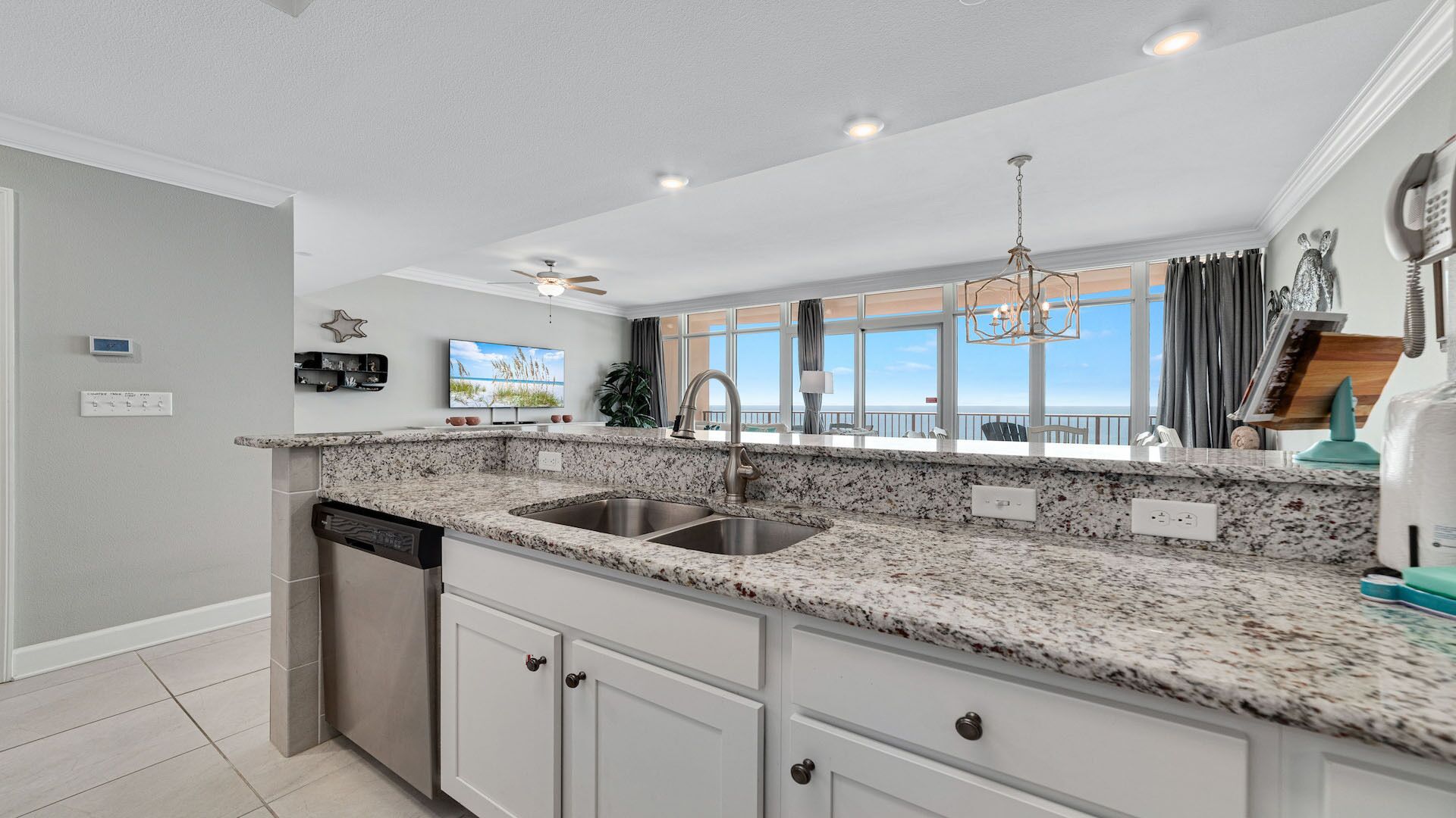 A modern kitchen with granite countertops, stainless steel appliances, and a view of the ocean through large windows.