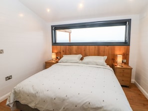 A bedroom with a large bed, wooden headboard, two bedside tables with lamps, and a window above the bed.