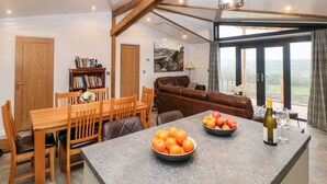 A spacious living area with a dining table, a sofa, and a kitchen island with fruit bowls. - Stables Lodge (Chesterfield)