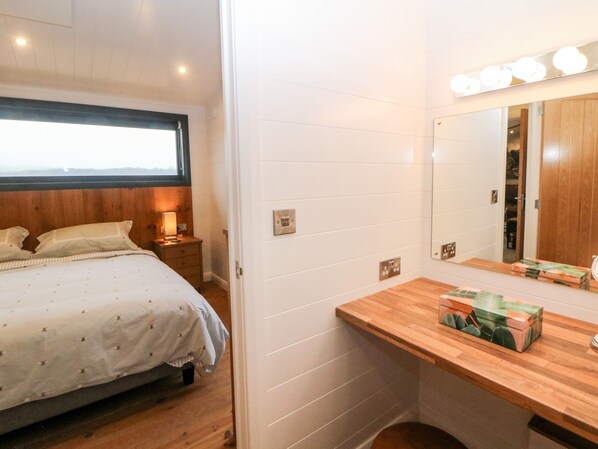 A bedroom with a bed, bedside table, lamp, and a mirror with lights above it.