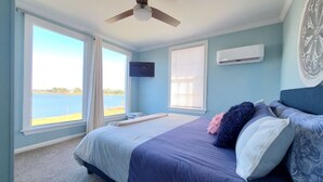 Une chambre avec un lit, un ventilateur de plafond, une télévision et une vue sur l’eau.