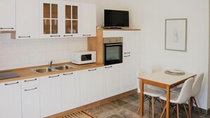 A modern kitchen with white cabinets, a microwave, an oven, and a dining area with a table and chairs. - Couple Getaway near Adriatic Sea (Biograd)