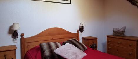 A bedroom with a wooden bed, two bedside tables, a nightstand, a lamp, a dresser, and a framed picture on the wall.