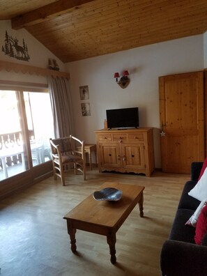 A living room with a wooden coffee table, a television on a wooden cabinet, a chair, and a couch.
