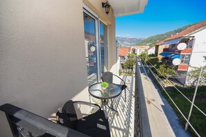 Een balkon met een glazen tafel en stoelen, een bloempot en uitzicht op een woonwijk met huizen en bergen op de achtergrond.