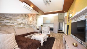 A modern living room with a stone wall, a fireplace, and a kitchen in the background.