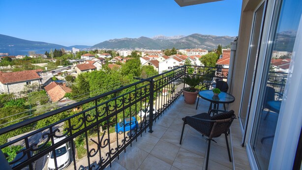 A balcony with a view of a town and mountains, a table with chairs, and a potted plant.