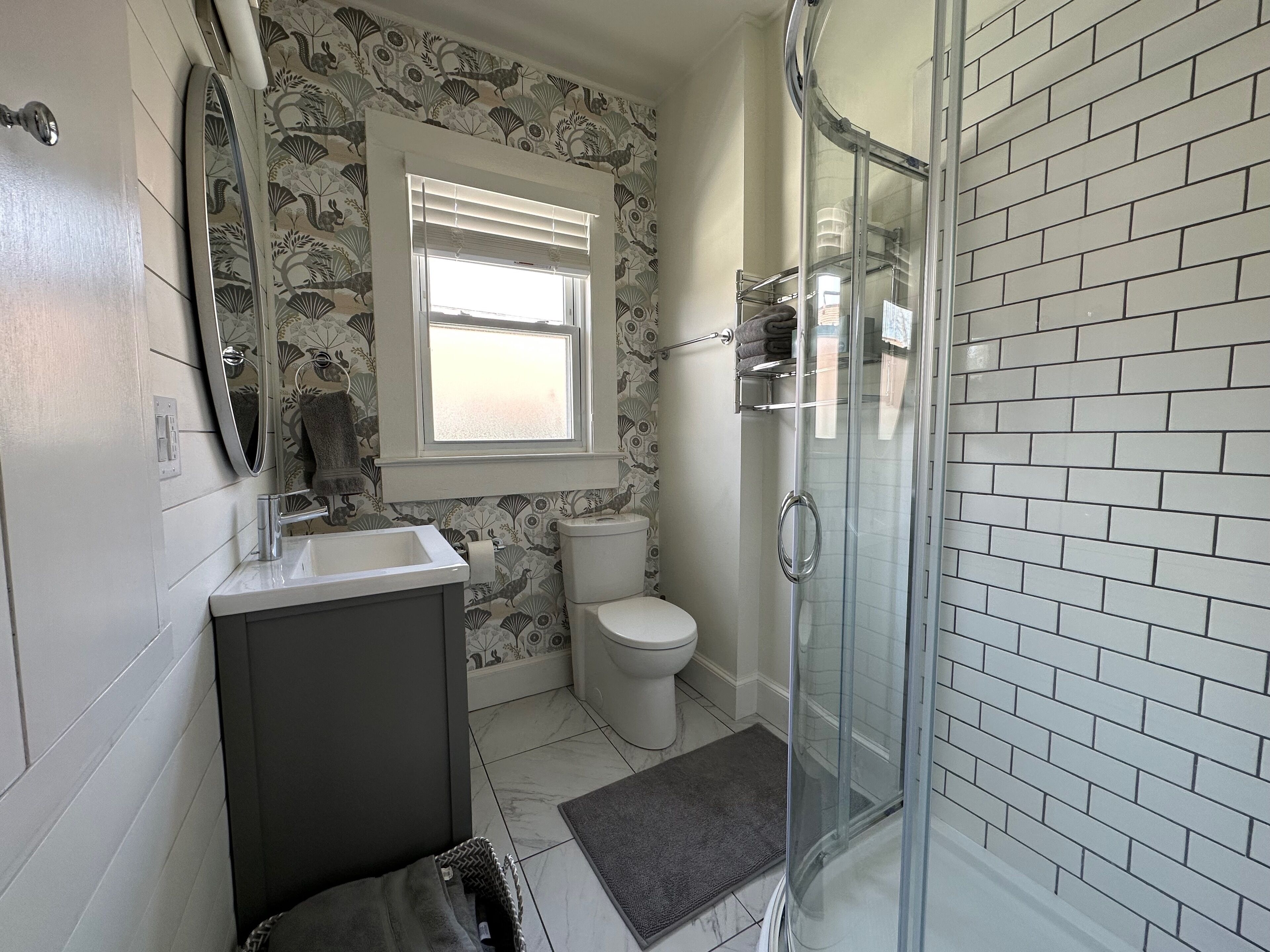 A bathroom with a shower, toilet, sink, and a window.