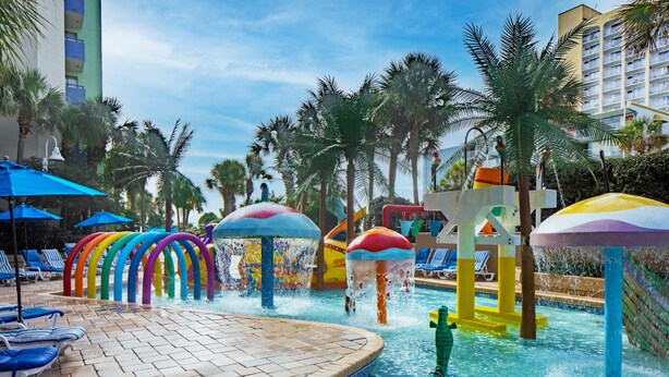 A pool area with colorful water features and lounge chairs. - Family Suite at Coral Beach Resort - Full Access to Amenities! (Myrtle Beach)