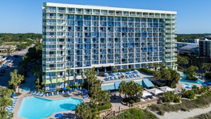 A high-rise hotel with multiple balconies, a swimming pool, and a beach area with sun loungers. - Family Suite at Coral Beach Resort - Full Access to Amenities! (Myrtle Beach)